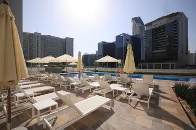 a pool with white lounge chairs and umbrellas at 1BR Facing Canal and City Views, Just a Short Walk to Bus Stop and Marine Transport, Reva Residences, Business Bay by Deluxe Holiday Homes in Dubai