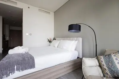 a white bedroom with a bed and a chair at Cozy studio with Burj Khalifa and canal view in Dubai