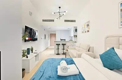a white living room with a white couch and a blue rug at Bloomfields Comfort Studio at Bali Residence, DXB in Dubai
