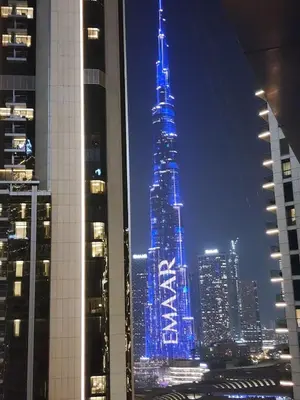 a tall skyscraper lit up in blue at night at Damac Maison Mall Street LARGE 2BR I Full Burj Views I Connects Dubai Mall in Dubai