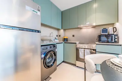 a kitchen with green cabinets and a washer and dryer at Just Moments from Coca-Cola Arena and Metro 1BR, Surrounded by a Vibrant Array of Retail and Dining Outlets, Viridian, Al Wasl by Deluxe Holiday Homes in Dubai
