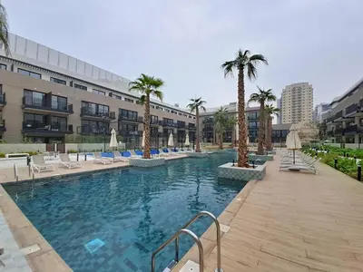 a pool with chairs and palm trees in a building at Vacationer l Peaceful Studio l Circle Mall l Greenery Community in Dubai