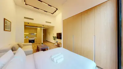 a bedroom with a white bed and a living room at Vacationer l Peaceful Studio l Circle Mall l Greenery Community in Dubai