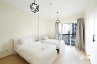 a white bedroom with two beds and a window at Brand New 2-BR Panoramic View - Near Marina & JBR in Dubai