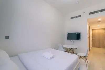 a white room with a bed and a table and a tv at Peaceful and Cozy Studio, Burj Khalifa View in Dubai