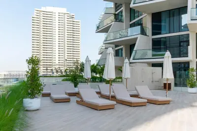 a patio with lounge chairs and umbrellas in front of a building at Elegant High-Floor Apartment with Pool in Dubai