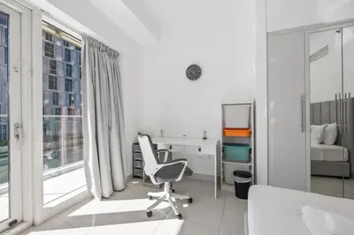 a white room with a chair and a desk and a window at Elite Escapes - Glamorous Damac Heights - 2 BR in Dubai