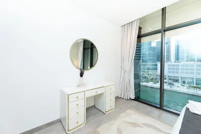 a white bedroom with a mirror and a desk at Escape24 Brand New 2BR with Canal Views near Burj Khalifa in Dubai