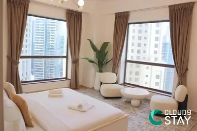 a bedroom with a white bed and two large windows at Cloud 9 - Steps to the Beach Elegant 2BR in JBR in Dubai