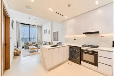 a kitchen with white cabinets and a living room at Cozy 1BR Retreat in Binghatti Amber JVC in Dubai