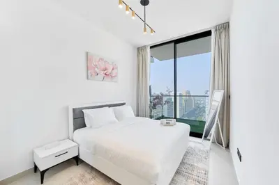 a white bedroom with a bed and a large window at Cozy 1BR Retreat in Binghatti Amber JVC in Dubai