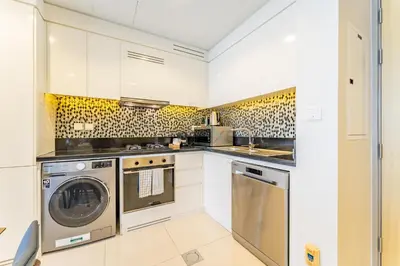 a kitchen with white cabinets and a washer and dryer at Minutes from Downtown Dubai and Burj Khalifa, Easy Metro Access, Seamless Connectivity to Marina and Palm Jumeirah - Aykon City 2 Tower C, Business Bay by Deluxe Holiday Homes in Dubai