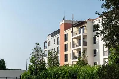 a white apartment building with trees in the foreground at Seaside 1-Bedroom Apartment with Beach Access at Port De La Mer in Dubai