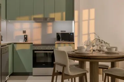 a kitchen with a wooden table with chairs and a kitchen with green cabinets at 1 Bedroom Apartment in Central Park, City Walk in Dubai