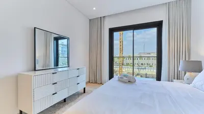 a white bedroom with a television and a large window at Stylish 1 Bedroom in Viridian City Walk in Dubai
