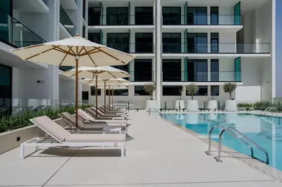 a pool with lounge chairs and umbrellas next to a building at Warm-Toned Studio with City Views in Binghatti Azure in Dubai