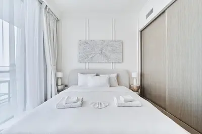 a white bedroom with a large white bed with two towels at 2BR Beachfront Apartment at Palace Beach Residence in Dubai
