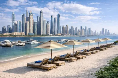 a beach with chairs and umbrellas in front of a city at 2BR Beachfront Apartment at Palace Beach Residence in Dubai