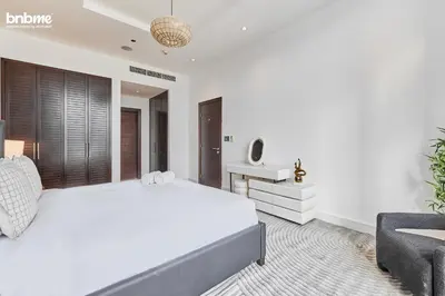 a white bedroom with a large bed and a chair at bnbmehomes - Tiara Residence in Dubai