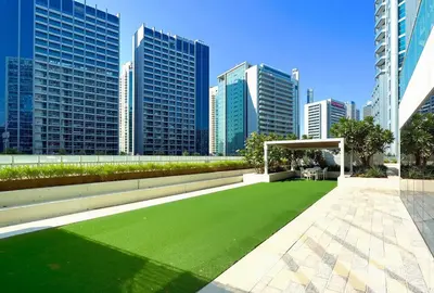 a green lawn in a city with tall buildings at Chic 1BR at Reva Stunning Canal Views in Dubai