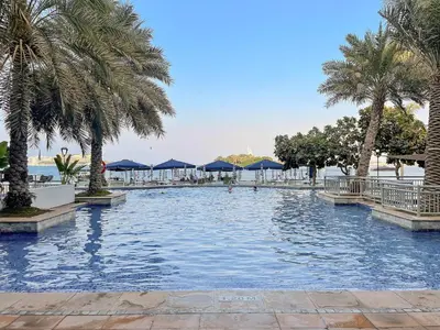a swimming pool with palm trees and blue umbrellas at VayK - Beachfront 1BR on Palm Jumeirah with Sea View in Dubai