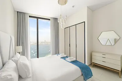 a white bedroom with a large bed and a window at VayK - Luxurious 2BR Beachfront Retreat with Ocean View in Dubai