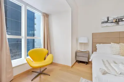 a bedroom with a yellow chair in front of a window at Vacay Lettings - Elite Residence - 1 BR - Partial Sea View in Dubai