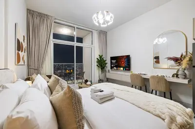 a white bedroom with a large bed and a table at Cozy Studio with 31st Floor Miracle Garden View in Dubai