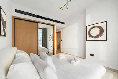a white bedroom with a bed and a mirror at New! Lovely 1BR with Balcony & Pool in Binghatti Orchid in Dubai
