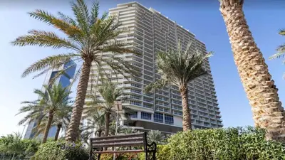 a tall building with palm trees in front of a bench at The Fitness Suite JVC - Pool View - Zaya Hameni in Dubai