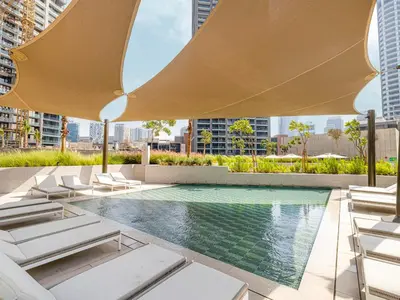 an infinity pool with lounge chairs and a large umbrella at Peninsula One Suites by Prestige Nest in Dubai