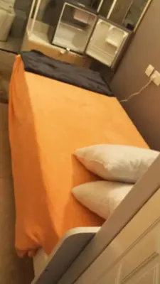 a bed with an orange sheet and pillows on it at Partition with attached washroom in Dubai