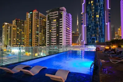a swimming pool with chairs and a city at night at Bloomfields STU in Business Bay, Bayz by Danube in Dubai