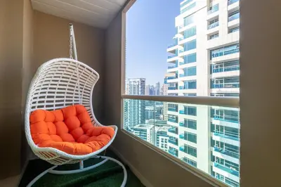 a white rattan chair in a balcony with a large window at Luxury 3BR & Floating Bed in Marina with Pool in Dubai