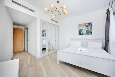 a white bedroom with a large white bed and a chandelier at Stunning 1BR Apartment with Breathtaking Marina Views in Dubai