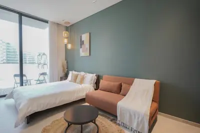 a bedroom with a bed and a couch and a window at Stylish modern studio near Miracle Garden with Gym, Pool and Padel court in Dubai