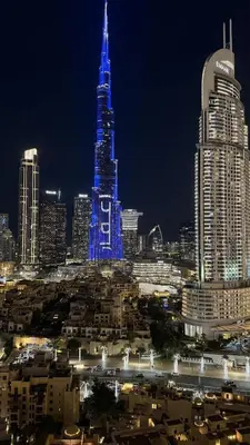 a city at night with a blue lit up building at Rentico l Ultra Luxury 2BR Burj Khalifa & Fountain in Dubai