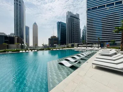 a large swimming pool with white lounge chairs in a city at Curated High Floor 1BR-Sofa Bed Water View Peninsula 1 in Dubai