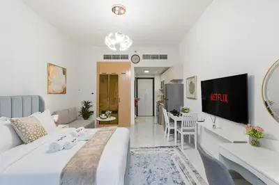 a living room with a white bed and a tv at Modern Studio on 27th Floor with Miracle Garden Views in Dubai