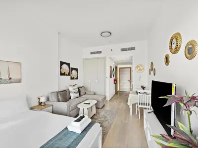 a white room with a bed and a living room at Spacious Studio w Sofa Bed Sleeps 4 in JVC in Dubai