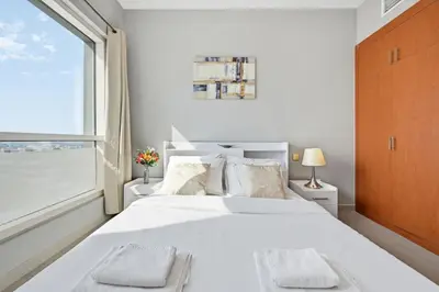 a white bedroom with a large bed and a window at Lake Point Tower 1 BHK by Petals Holiday Homes in Dubai