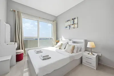 a bedroom with a white bed with a large window at Lake Point Tower 1 BHK by Petals Holiday Homes in Dubai