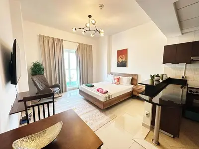 a living room with a bed and a table and a kitchen at Comfortable Studio Retreat in Dubai Sports City in Dubai
