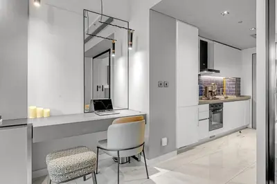 a white kitchen with a desk and a chair at Chic Studio Steps to Dubai Mall with Infinity Pool in Dubai