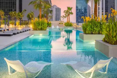 a swimming pool with two white chairs in a building at Vogue Downtown The Sterling by Omniyat, near Burj Khalifa and Dubai Mall, Studio Apartment with Balcony and Access to all Amenities in Dubai