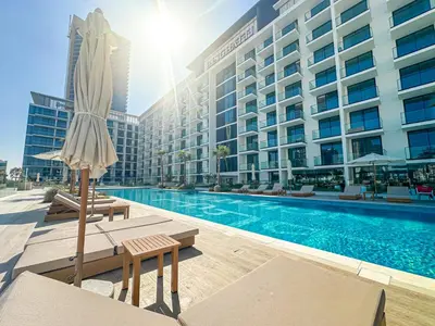 a hotel swimming pool with an umbrella and a hotel at WelHome - Urban Comfort Studio in JVC in Dubai