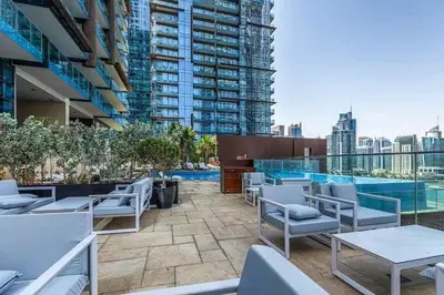 a rooftop patio with chairs and tables and a pool at Vogue Marina Gate near JBR Beach and Marina Mall, One Bedroom Apartment with Balcony and city skyline view, Access to all Amenities in Dubai
