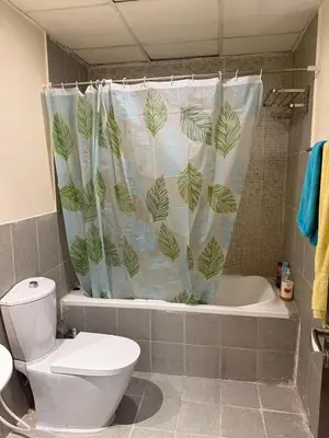 a bathroom with a toilet and a shower curtain with leaves at Modern 1BR in JVC, 2 Baths, Pool & Gym, Fully Equipped Kitchen in Dubai