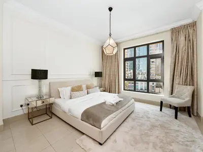 a white bedroom with a large bed and a chair at Skyline Select 1 Bedroom Apartment I Burj Khalifa View I Souk Al Bahar Downtown I Parking, Gym, Wi-Fi & Pool in Dubai