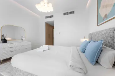 a white bedroom with a large white bed with blue pillows at StayShort - Chic Discovery Gardens 1Bed that Sleeps 2 in Dubai